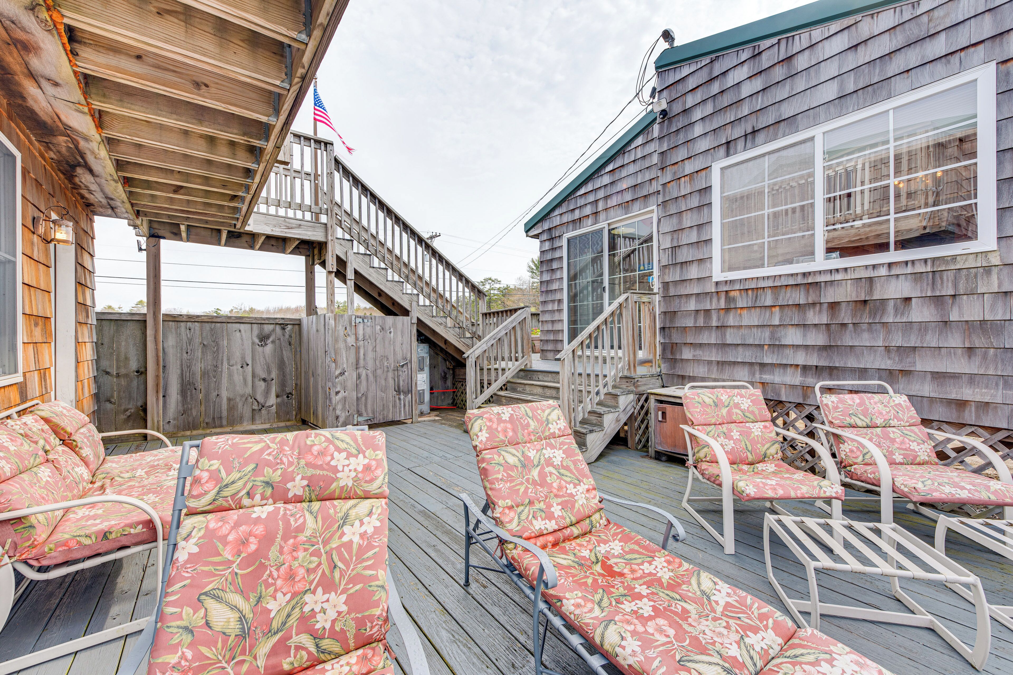 A wooden deck with lounge chairs and a staircase leading to a deck.
