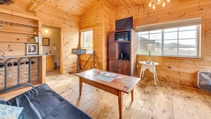 Interior acogedor de una cabaña con techo de madera, zona de comedor con mesa y sillas, una pequeña kitchenette y un amplio ventanal con vistas.
