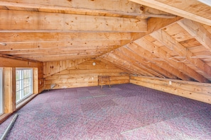 Une chambre mansardée avec des poutres en bois, une fenêtre et un plancher recouvert de moquette.