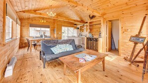 Interior de una cabaña de madera con sofá, mesa de comedor y un cuadro sobre caballete.