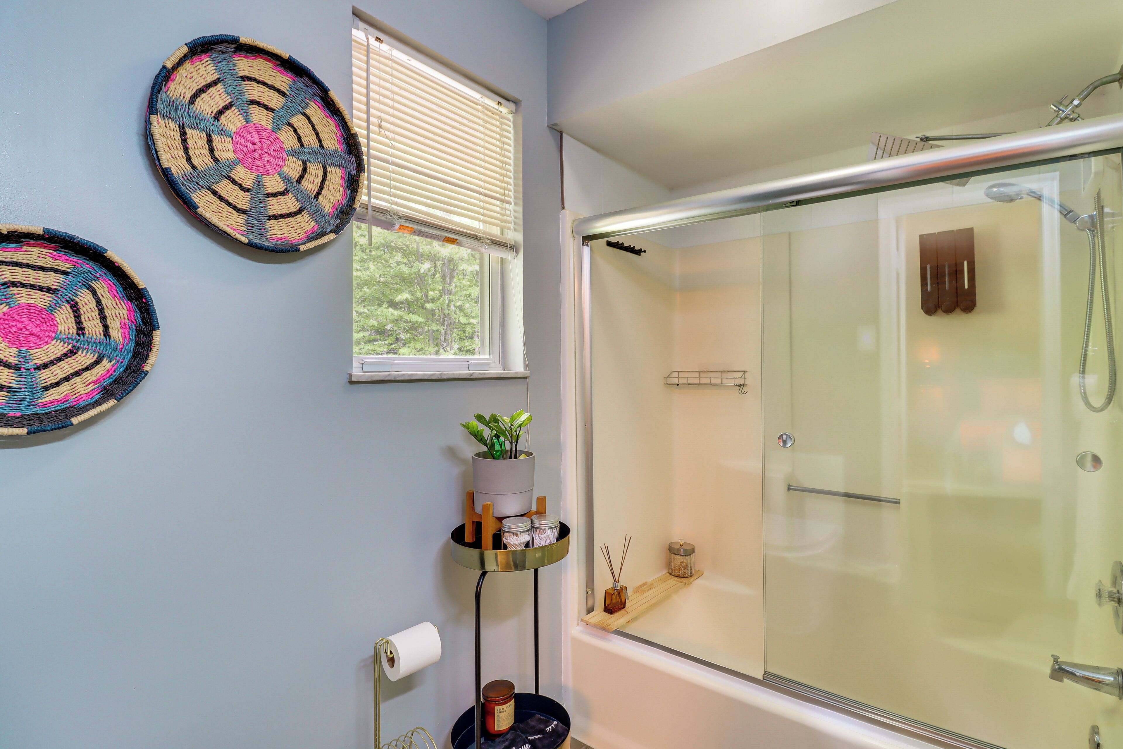 Een badkamer met een douchecabine van glas, een toiletrolhouder en een klein plankje met een potplant en twee potten.