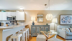 A modern kitchen with white cabinets, a stainless steel microwave, and a bar area with stools.