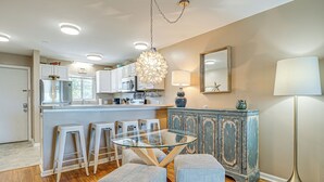 A modern kitchen with white cabinets, a stainless steel refrigerator, and a glass-top dining table with bar stools.