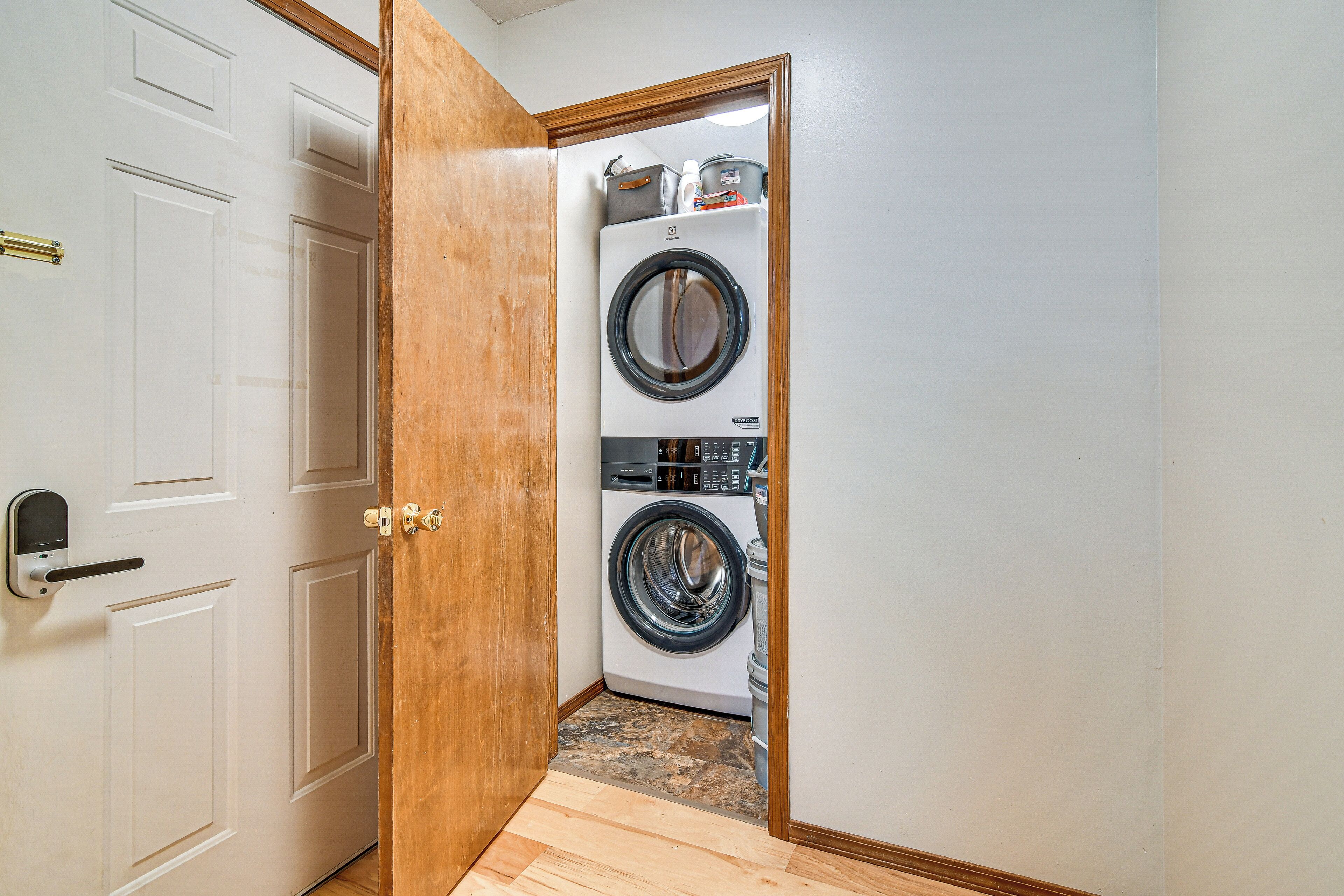 A laundry room with a front-loading washer and dryer, a wooden door, and a tiled floor.