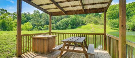 A wooden deck with a picnic table and a hot tub, overlooking a grassy area and a body of water.