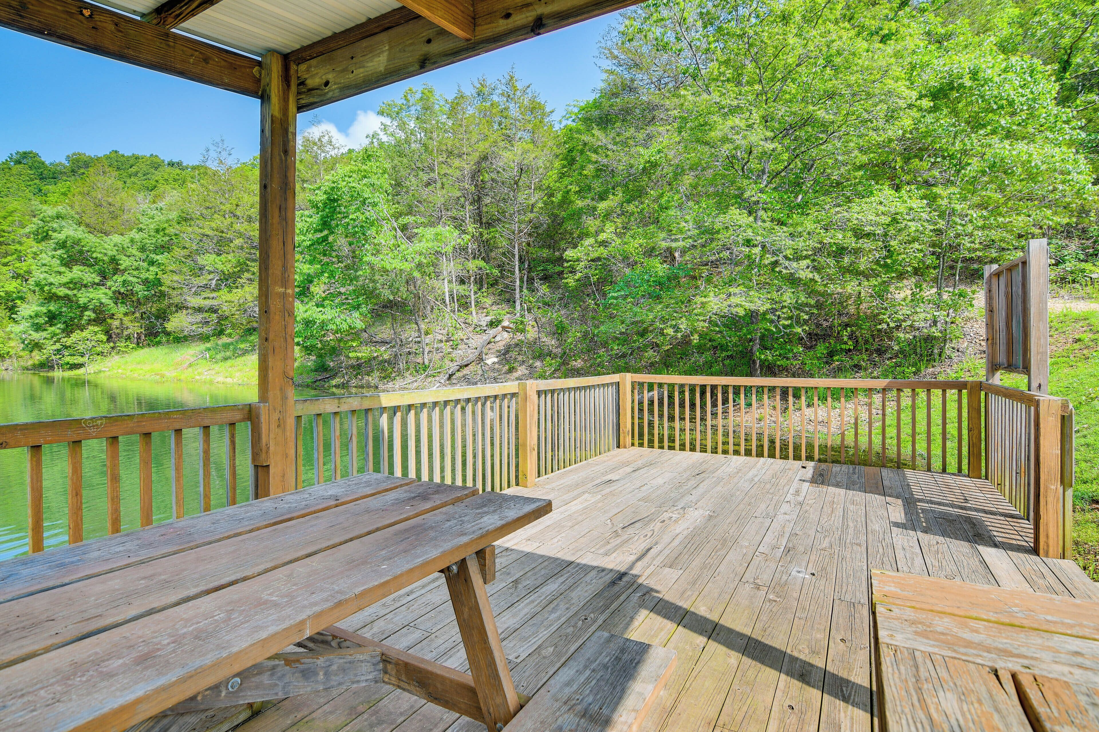 A wooden deck with a picnic table and a railing overlooking a forested area and a body of water.