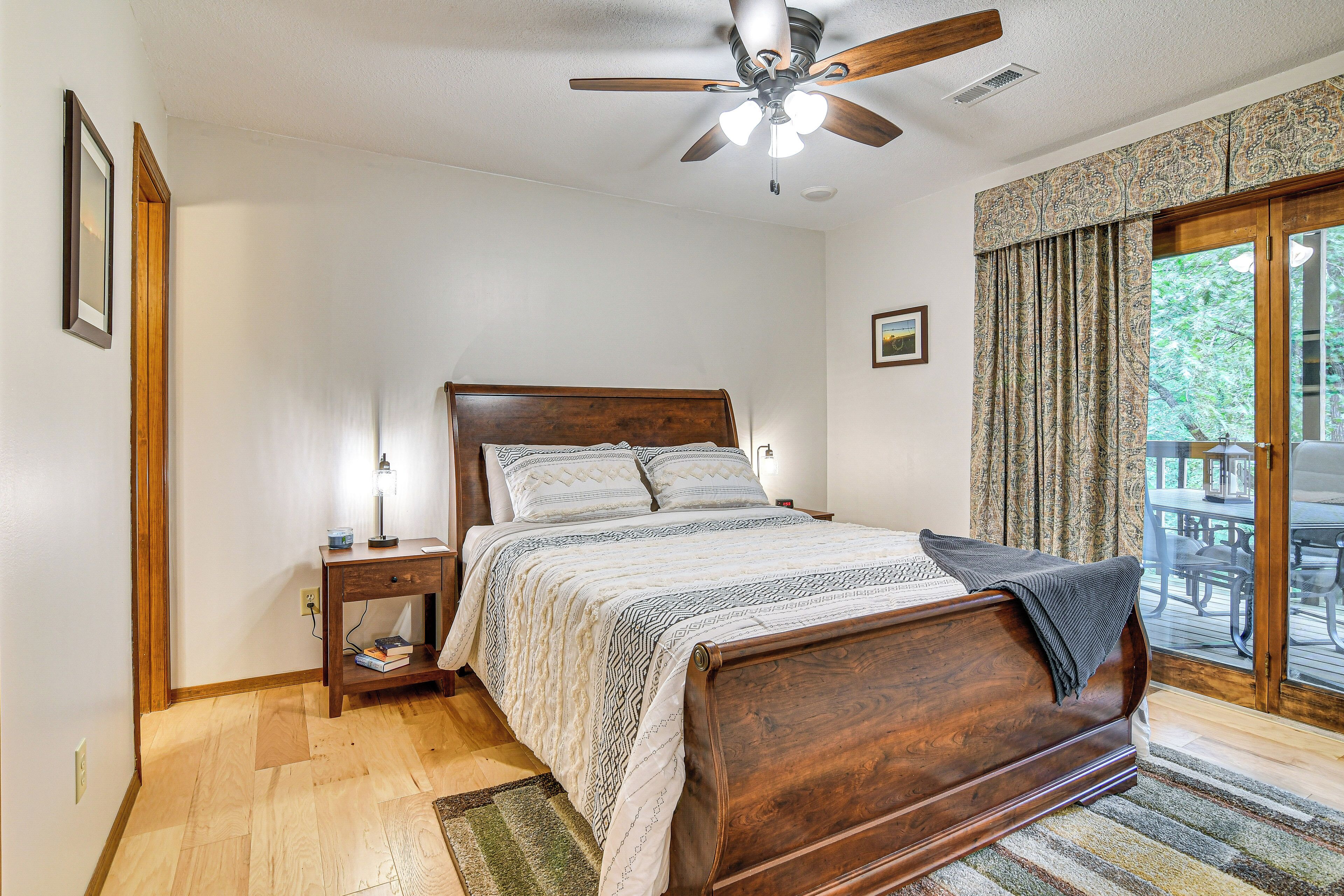 A bedroom with a wooden bed, a nightstand, a ceiling fan, and a view of the outdoors through a glass door.