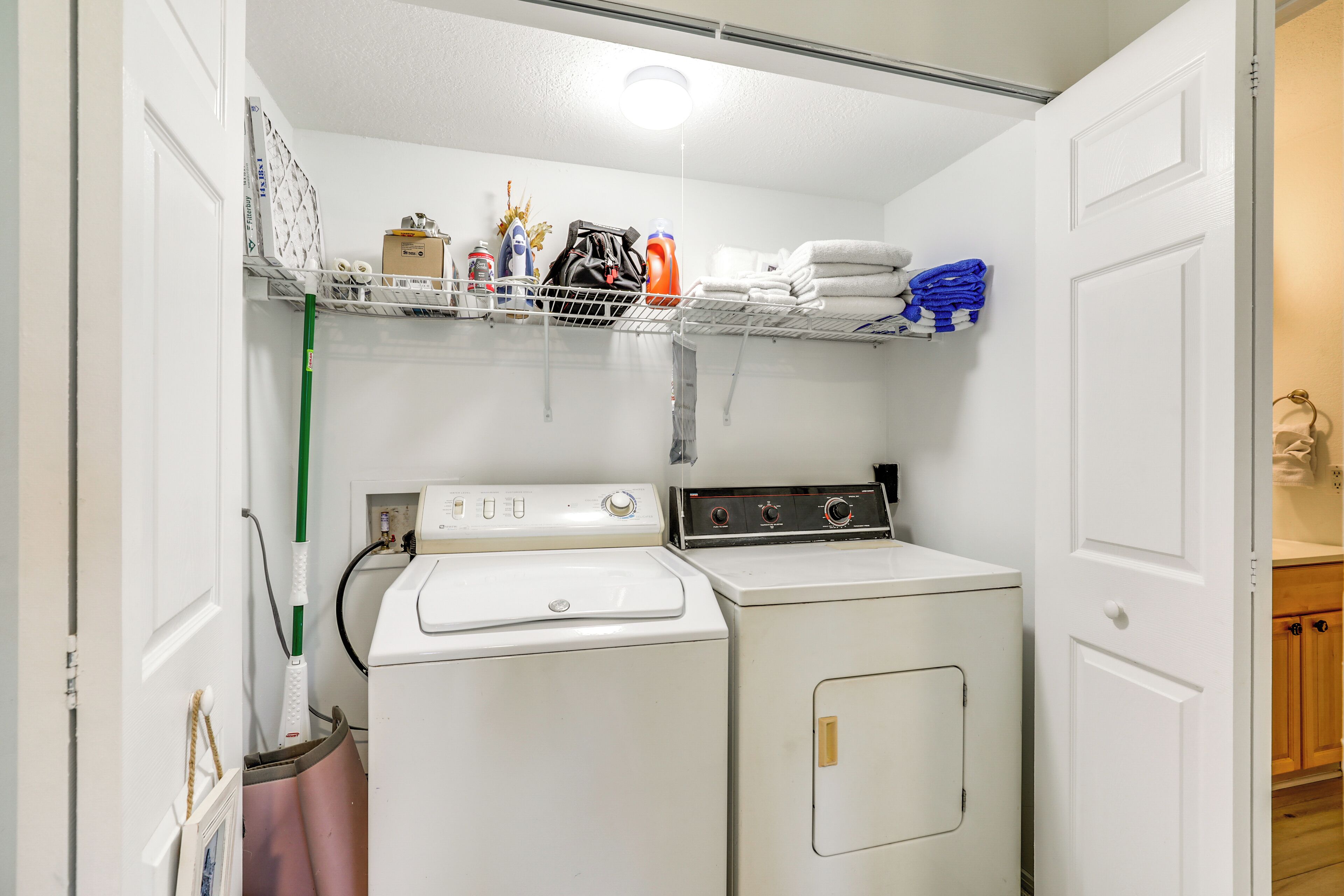 A laundry room with a washing machine, dryer, shelves with folded towels, and cleaning supplies.