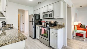 A modern kitchen with white cabinets, stainless steel appliances, and a granite countertop. - Walk to Pier: St Augustine Beach Condo w/ Balcony! (St. Augustine)