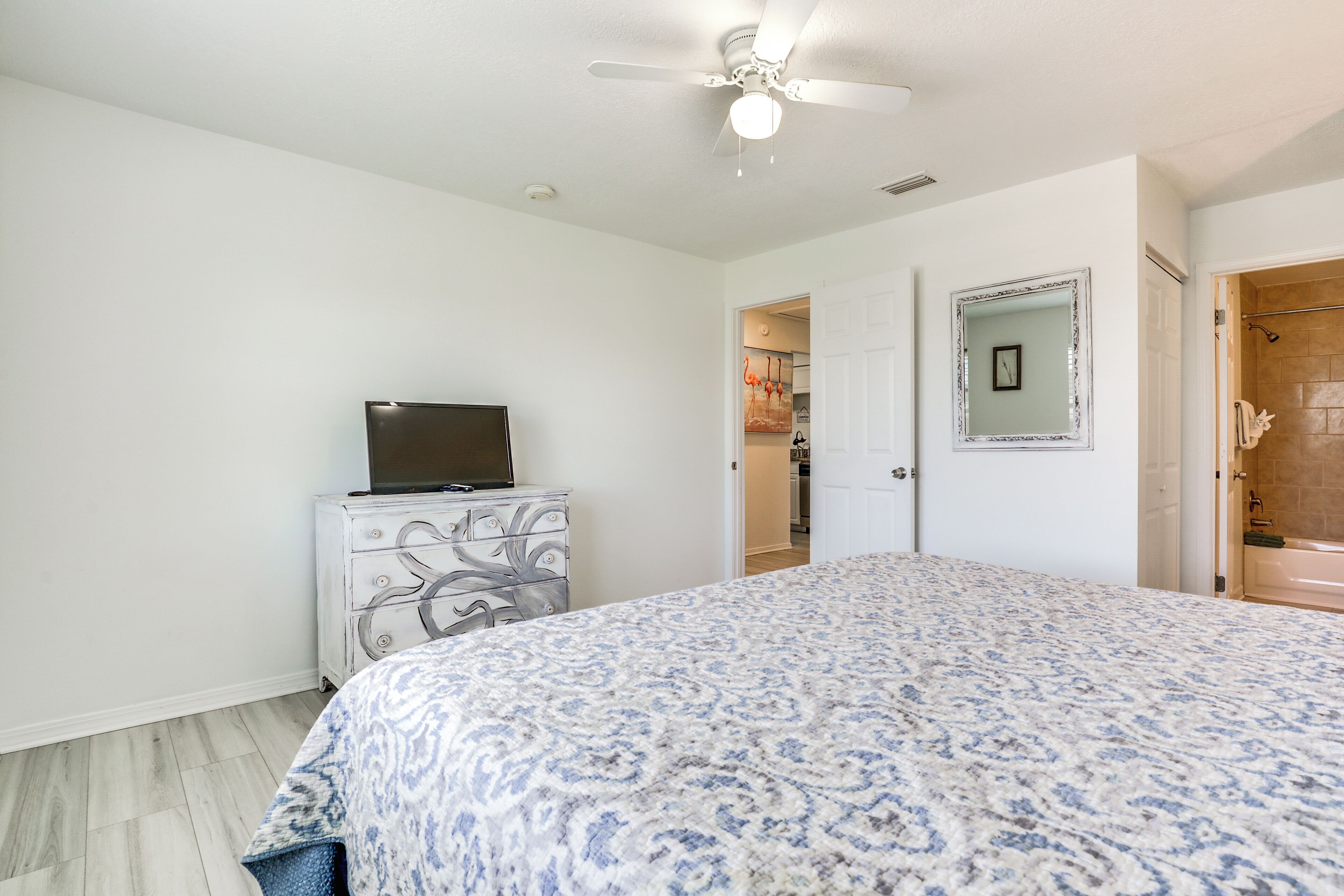 A bedroom with a bed, a dresser, a television, a ceiling fan, and a bathroom door.