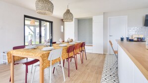 A dining area with a table set for four, two hanging pendant lights, and a kitchen area with a countertop and chairs. - New house- 6 adults & 4 children - 350m beach (Noirmoutier-en-l´Ile)