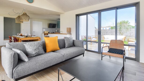 A modern living room with a grey sofa, a black coffee table, and a wicker chair. There is a large window with a view of the outside. - New house- 6 adults & 4 children - 350m beach (Noirmoutier-en-l´Ile)