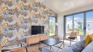 A modern living room with a large TV, a wooden cabinet, a black coffee table, and a sofa with cushions. - New house- 6 adults & 4 children - 350m beach (Noirmoutier-en-l´Ile)