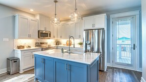 A modern kitchen with white cabinets, a blue island, stainless steel appliances, and pendant lighting.