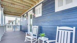 A covered porch with white rocking chairs and a small table, wooden ceiling beams, and a blue wall.