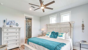A bedroom with a large bed, a dresser, a ceiling fan, and a window.
