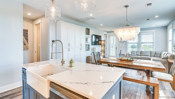 A modern kitchen with a large island, white cabinetry, and a dining area with wooden tables and benches.