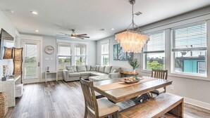 A spacious living area with a large wooden dining table, a sofa set, and a chandelier.