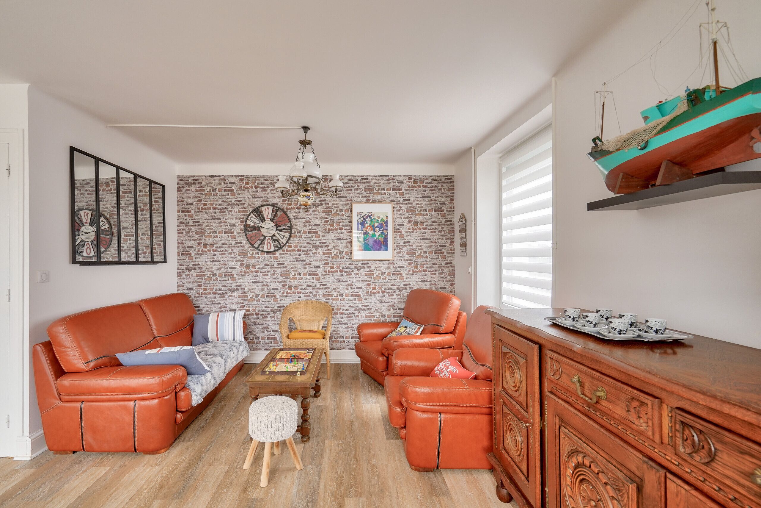 A living room with a brick wall, two leather sofas, a wooden coffee table, a wicker chair, and a wooden cabinet.