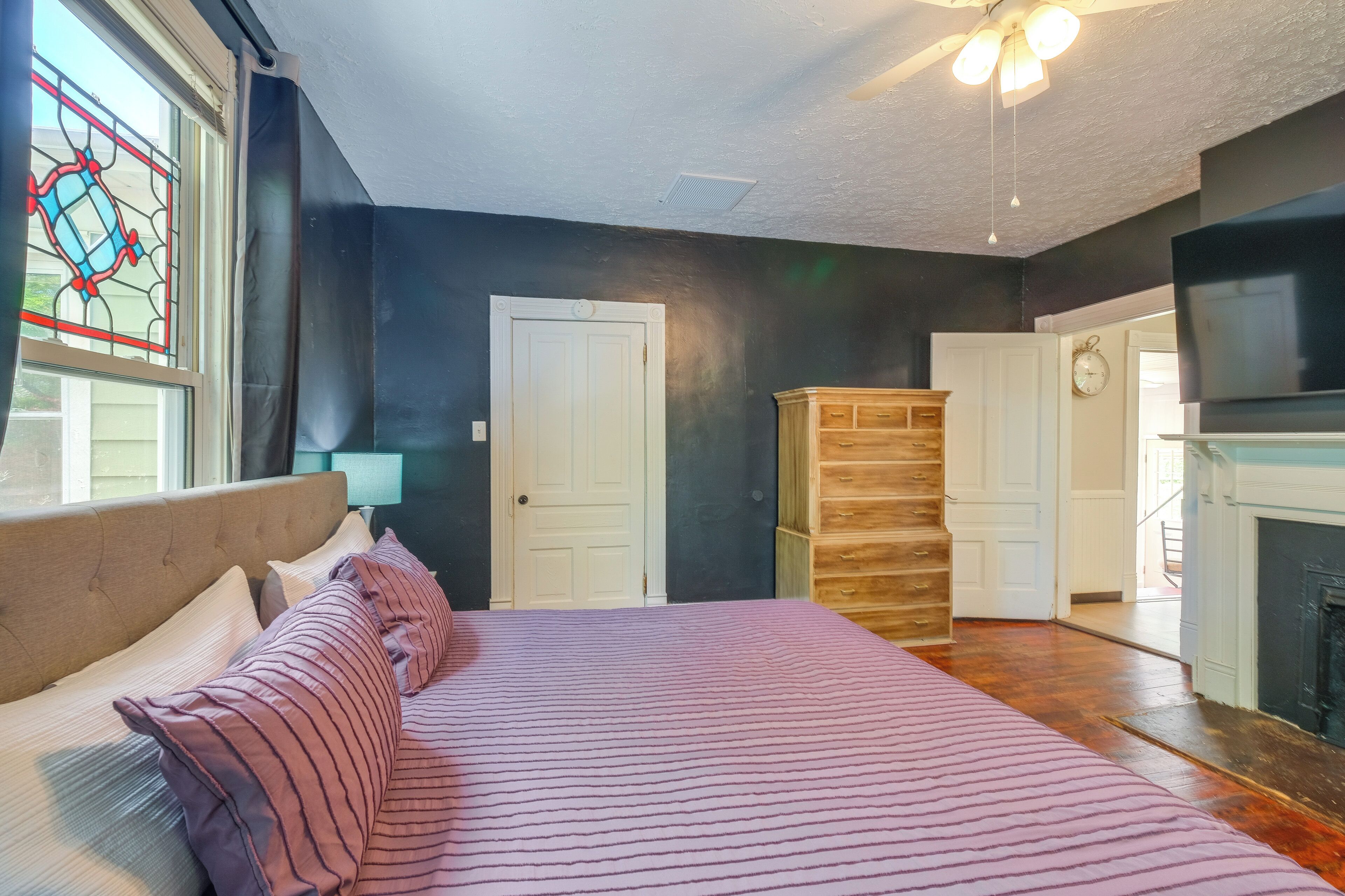 A bedroom with a bed, a dresser, a clock, and a fireplace.