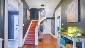 A hallway with a wooden staircase, a desk with plants, and a painting on the wall. - Walk to U of Lynchburg: Big Home w/ Yard & Hot Tub (Lynchburg)