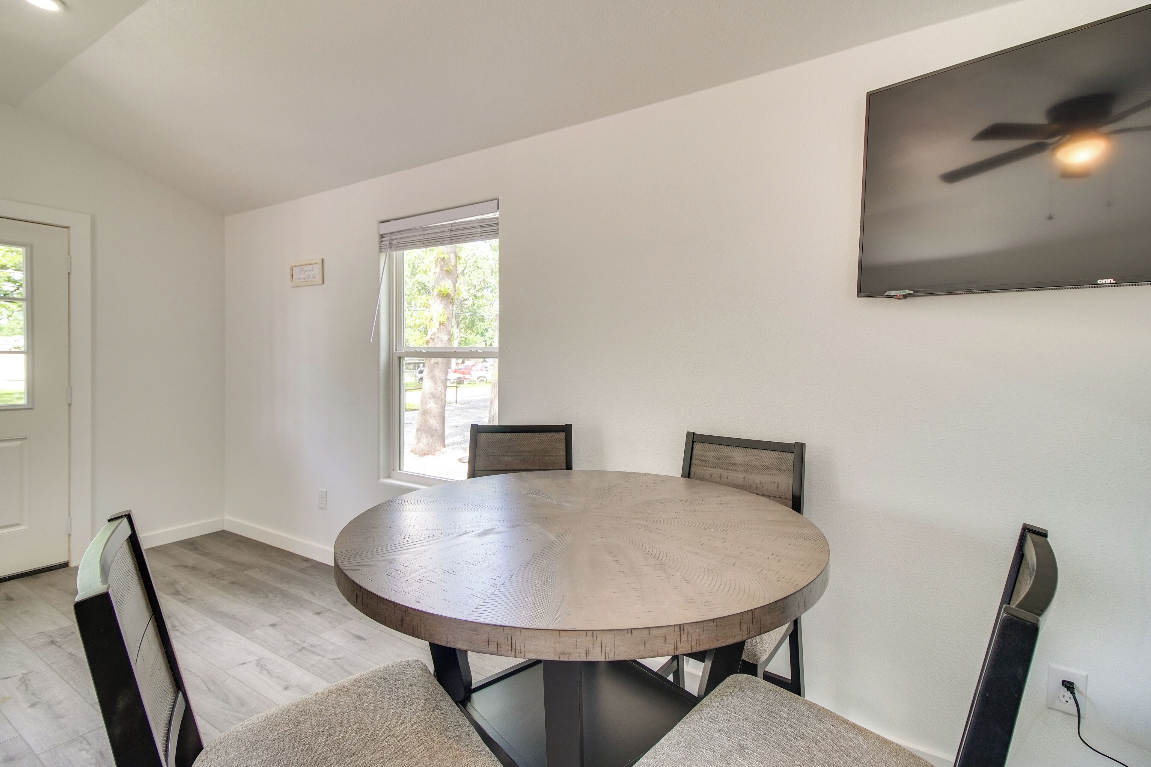 A round dining table with four chairs, a ceiling fan, and a window with blinds.