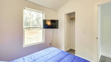 Un dormitorio con cama, televisión montada en la pared y ventana con vista a árboles.