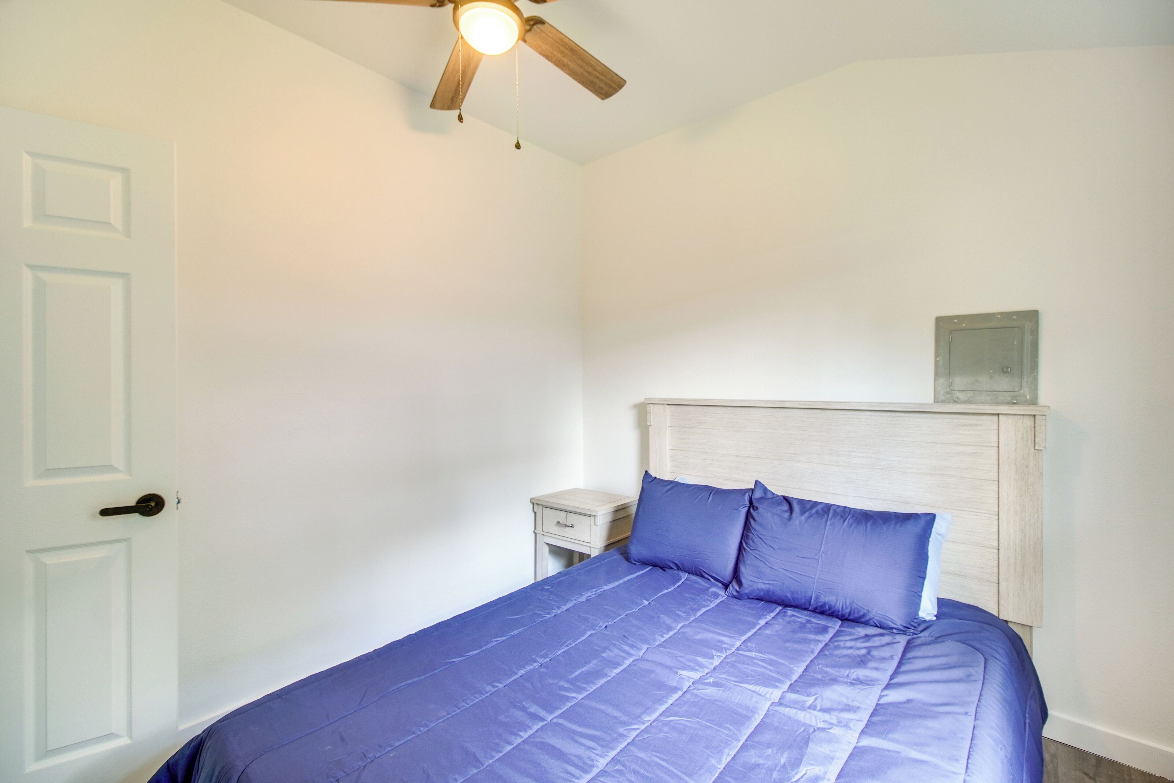 Une chambre à coucher avec un lit, une table de chevet, un ventilateur de plafond et une porte.