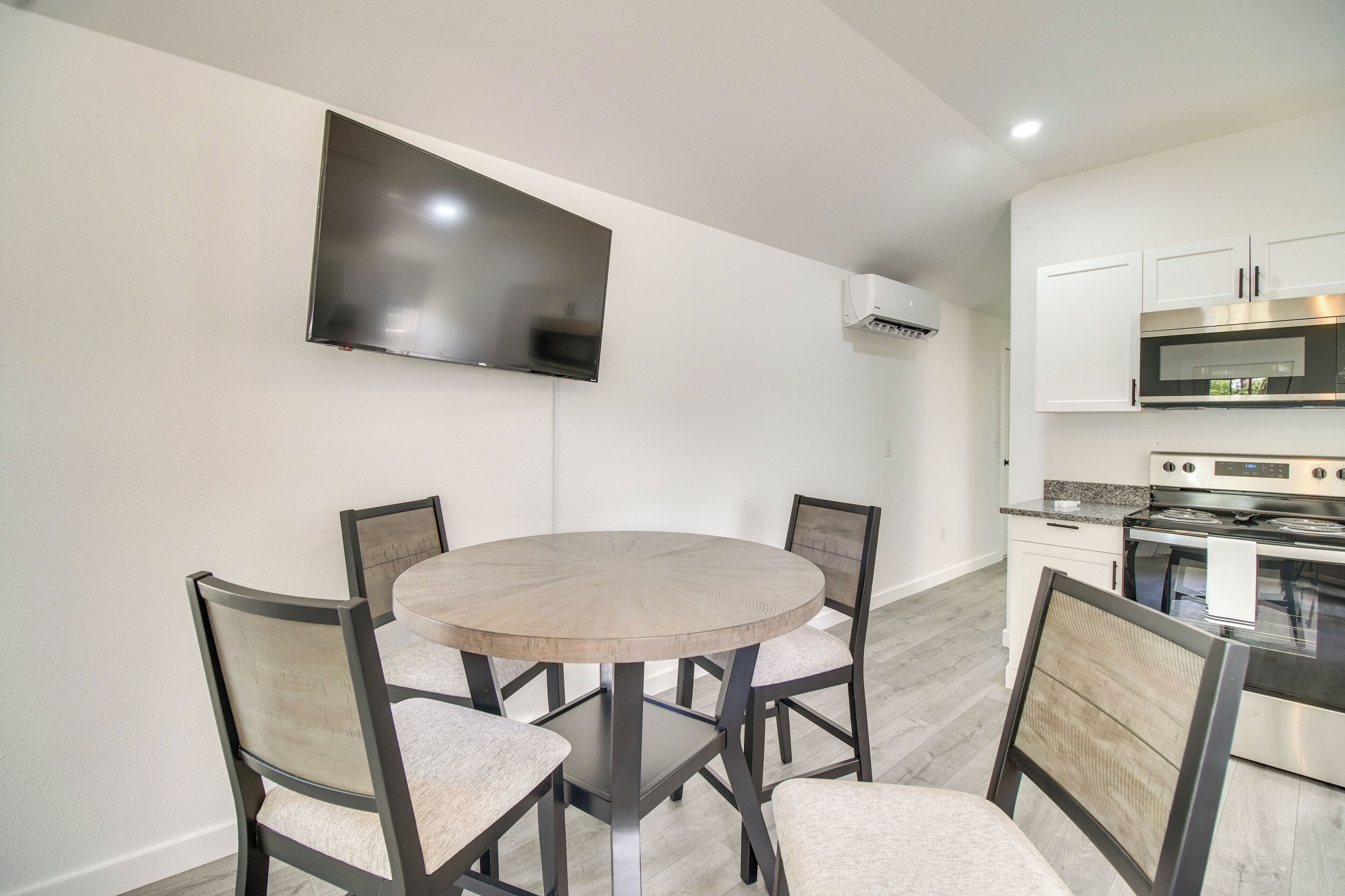 Una cocina moderna con un televisor de pantalla plana montado en la pared, una mesa de comedor con cuatro sillas y electrodomésticos integrados.