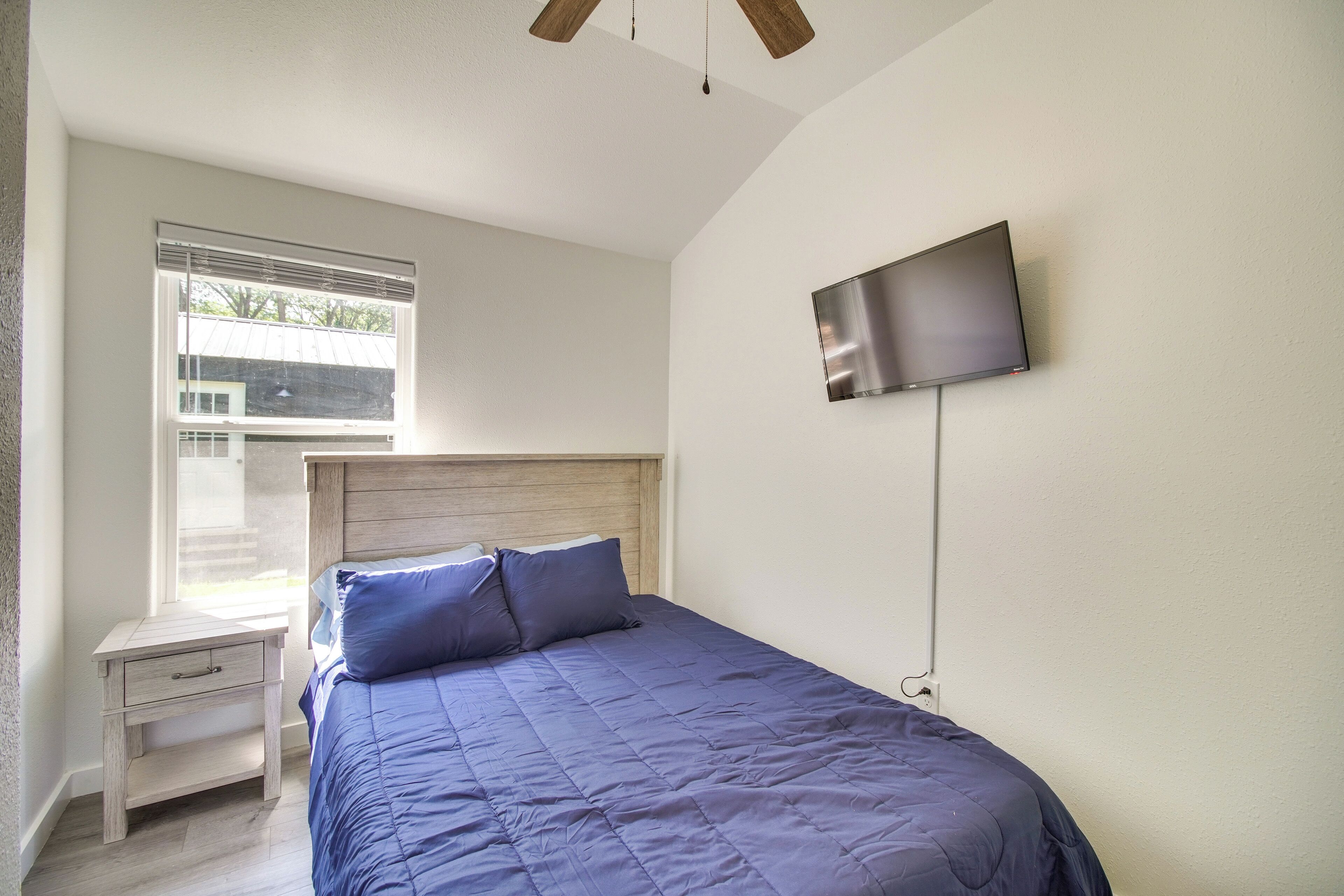 A bedroom with a bed, a nightstand, a TV mounted on the wall, and a window with blinds.