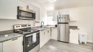A modern kitchen with white cabinets, stainless steel appliances, granite countertops, and a small trash bin. - Walk to Lake: Cozy Grove Cabin w/ Fire Pit (Grove)