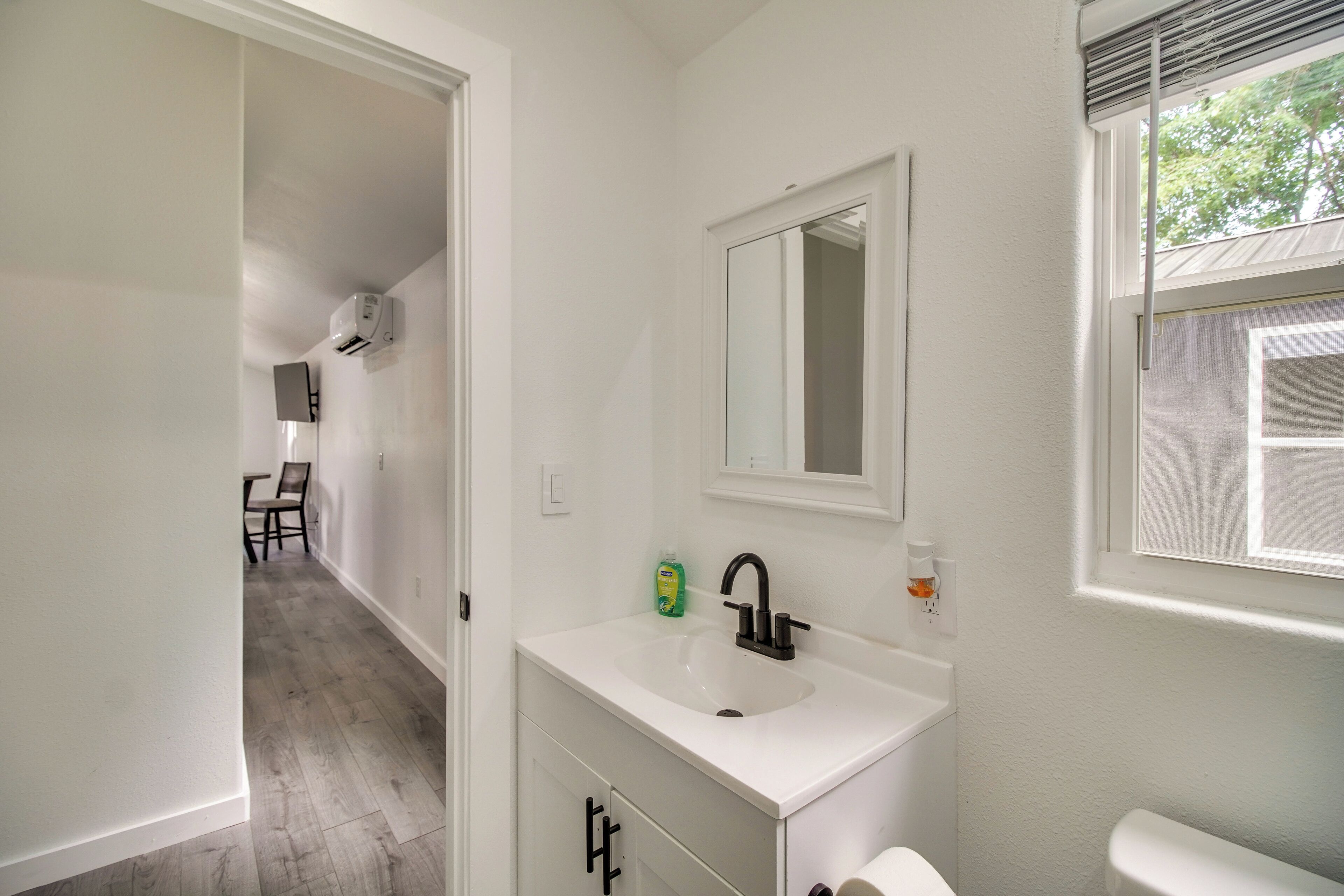 A bathroom with a white sink, a mirror, and a window.
