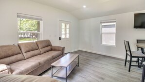 A spacious living room with a brown leather sofa, a wooden coffee table, and a dining area with a table and chairs. - Walk to Lake: Cozy Grove Cabin w/ Fire Pit (Grove)