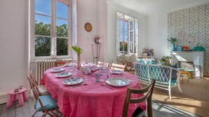 Un coin repas avec une table ronde dressée pour six personnes, entourée de chaises en bois dotées de coussins bleus.