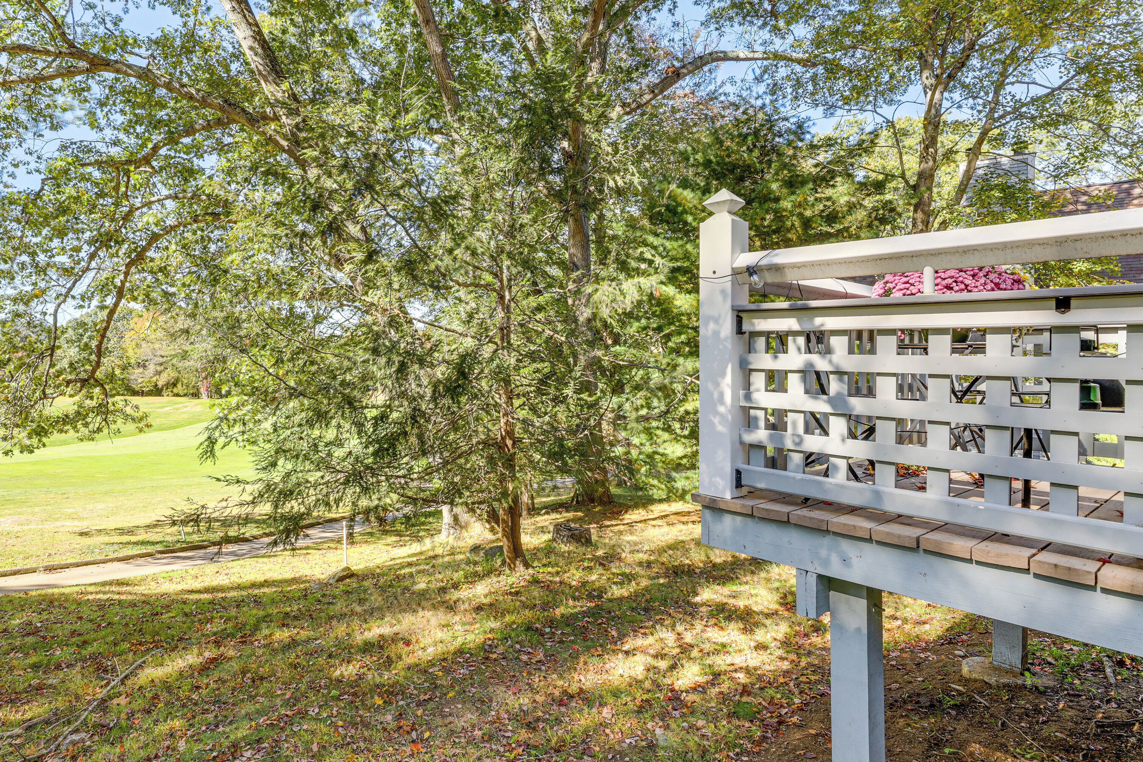 A white wooden bench with a lattice backrest and a flower box, situated in a park with trees and a grassy area.