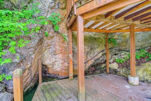 A wooden deck with a stone wall backdrop, surrounded by greenery. - Peaceful South Holston Lake Cabin w/ Dock & Deck! (Abingdon)