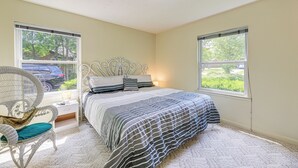 A bedroom with a bed, a chair, a nightstand, and two windows. - Morehead City Home ~ Walk to Beach Park! (Morehead City)