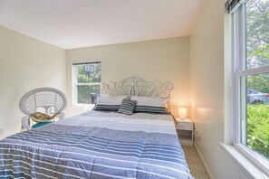 A bedroom with a bed, a chair, a nightstand, and a window.