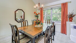A dining room with a wooden table, six chairs, a chandelier, a large mirror, and a window with curtains. - Morehead City Home ~ Walk to Beach Park! (Morehead City)