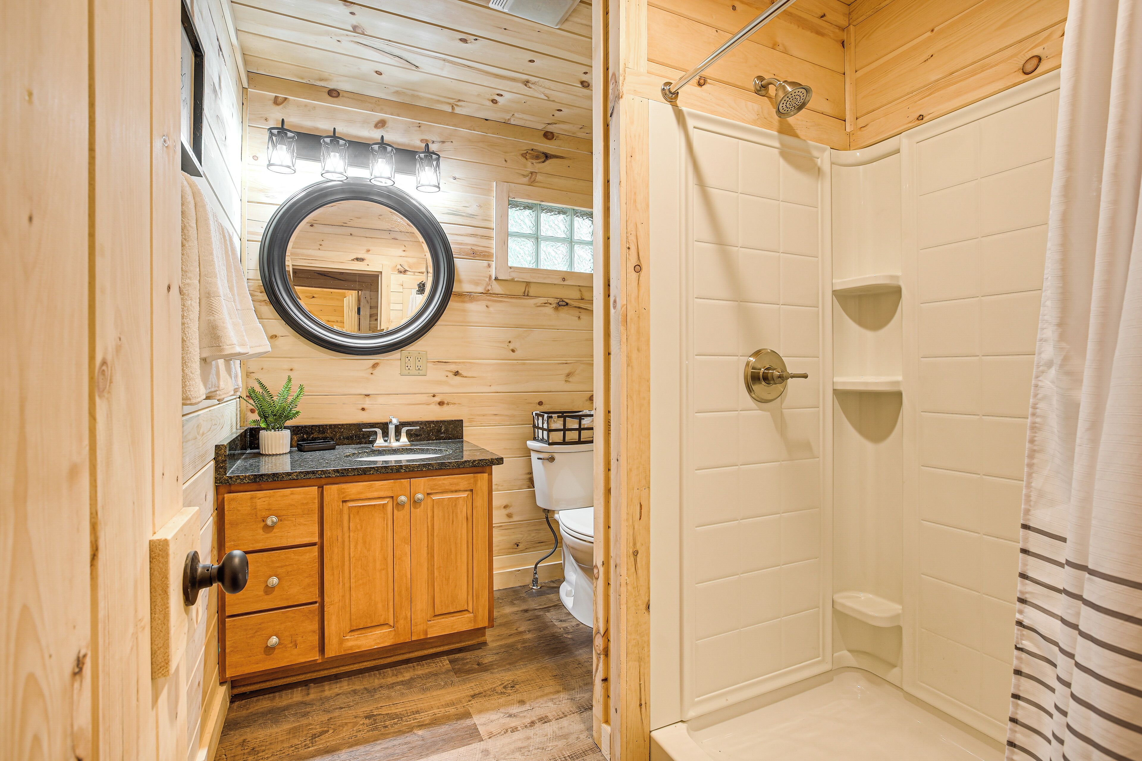 A wooden cabin bathroom with a sink, mirror, toilet, and shower.