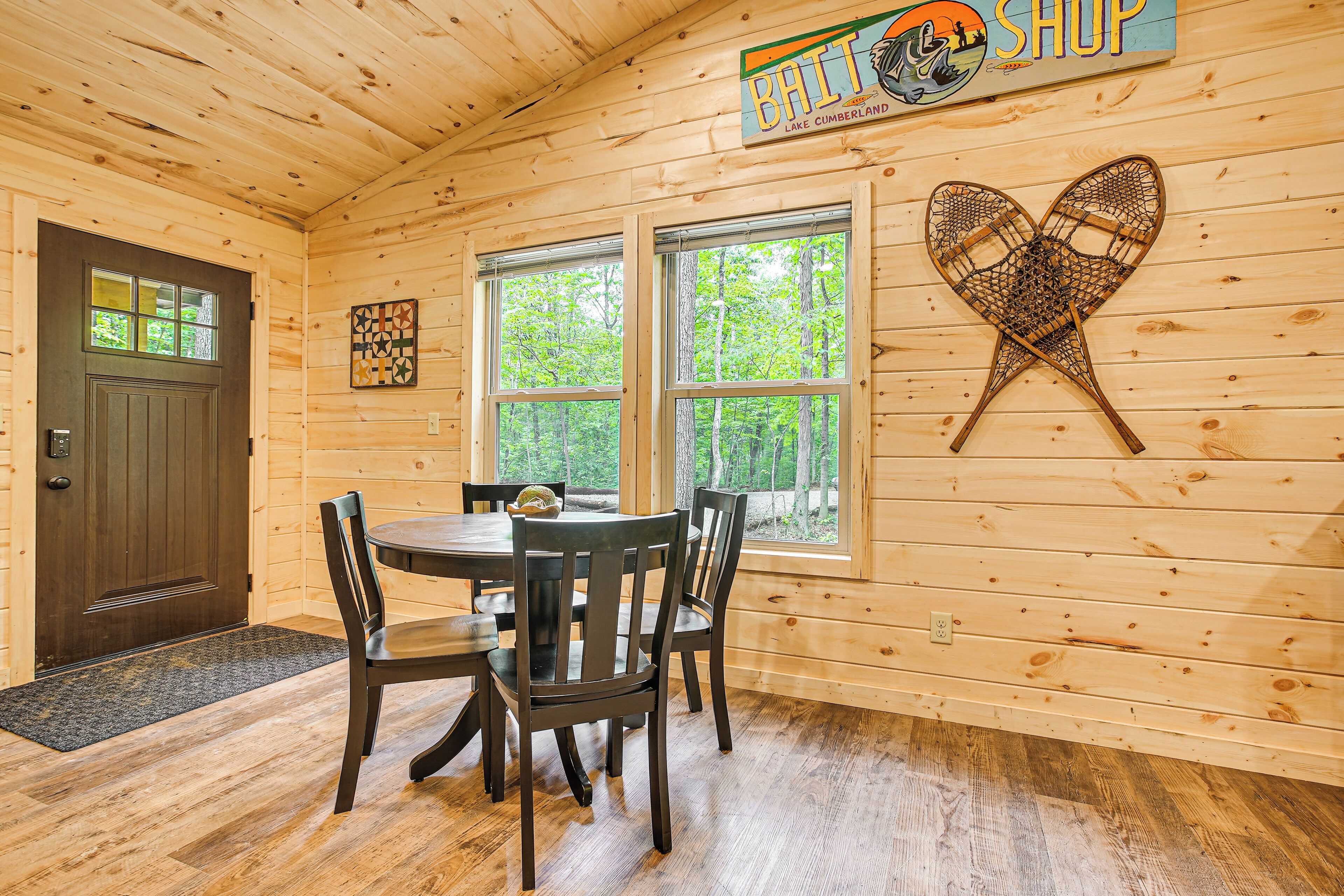 A wooden interior with a dining table, chairs, a door, windows, and a wall sign.