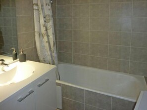 A bathroom with a bathtub, a sink with a mirror, and a shower curtain. - 50m from ski slopes, 3rd floor, balcony, 40m², Les Orres (Les Orres)