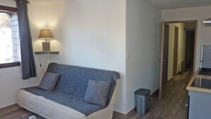 A modern living room with a sofa, a lamp, a trash bin, and a kitchen area in the background. - 3rd floor, balcony, 40m², Les Orres (Les Orres)