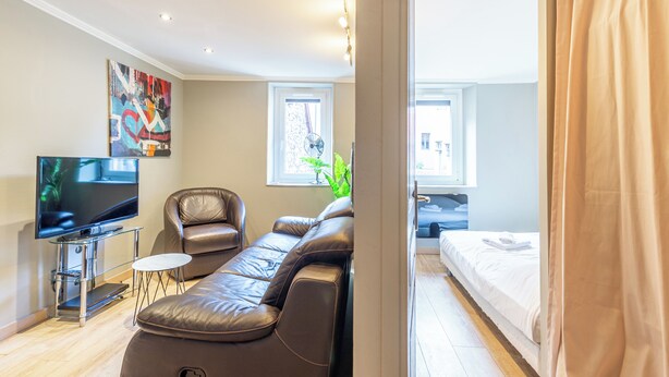 Un salon moderne avec un canapé en cuir, un téléviseur à écran plat, une petite table et un ventilateur.