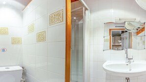 Une salle de bain avec des carreaux blancs, des toilettes, un lavabo et une douche.