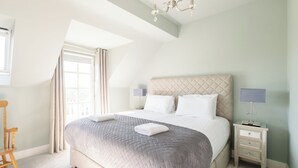 Une chambre à coucher avec un grand lit, une table de chevet, une chaise et une fenêtre avec des rideaux.