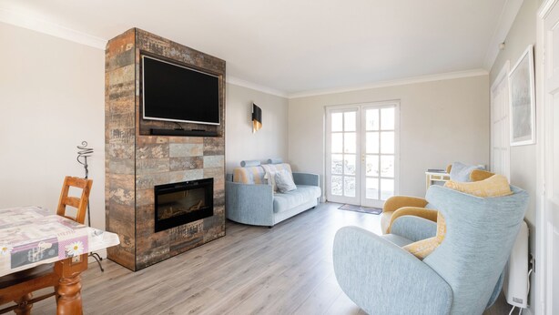 Un salon avec une cheminée, un canapé, un téléviseur fixé au mur en pierre et un coin repas avec une table et des chaises.