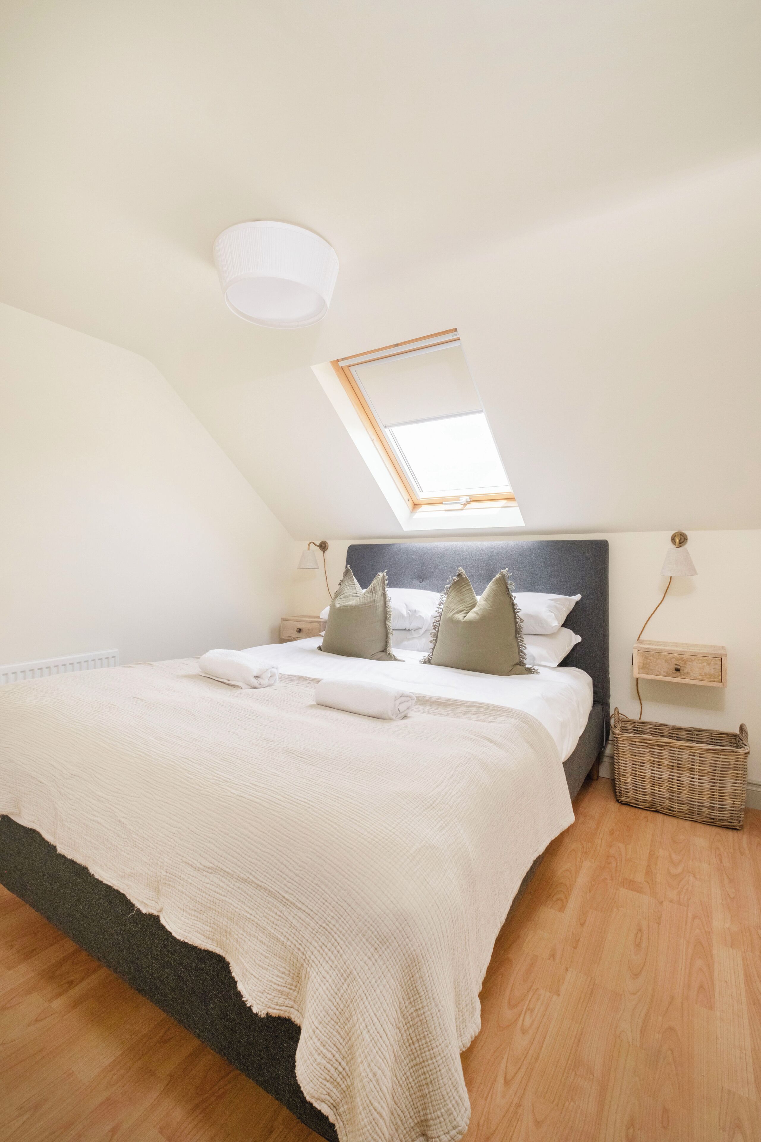 A bedroom with a skylight, a bed with pillows, a bedside table, and a lamp.