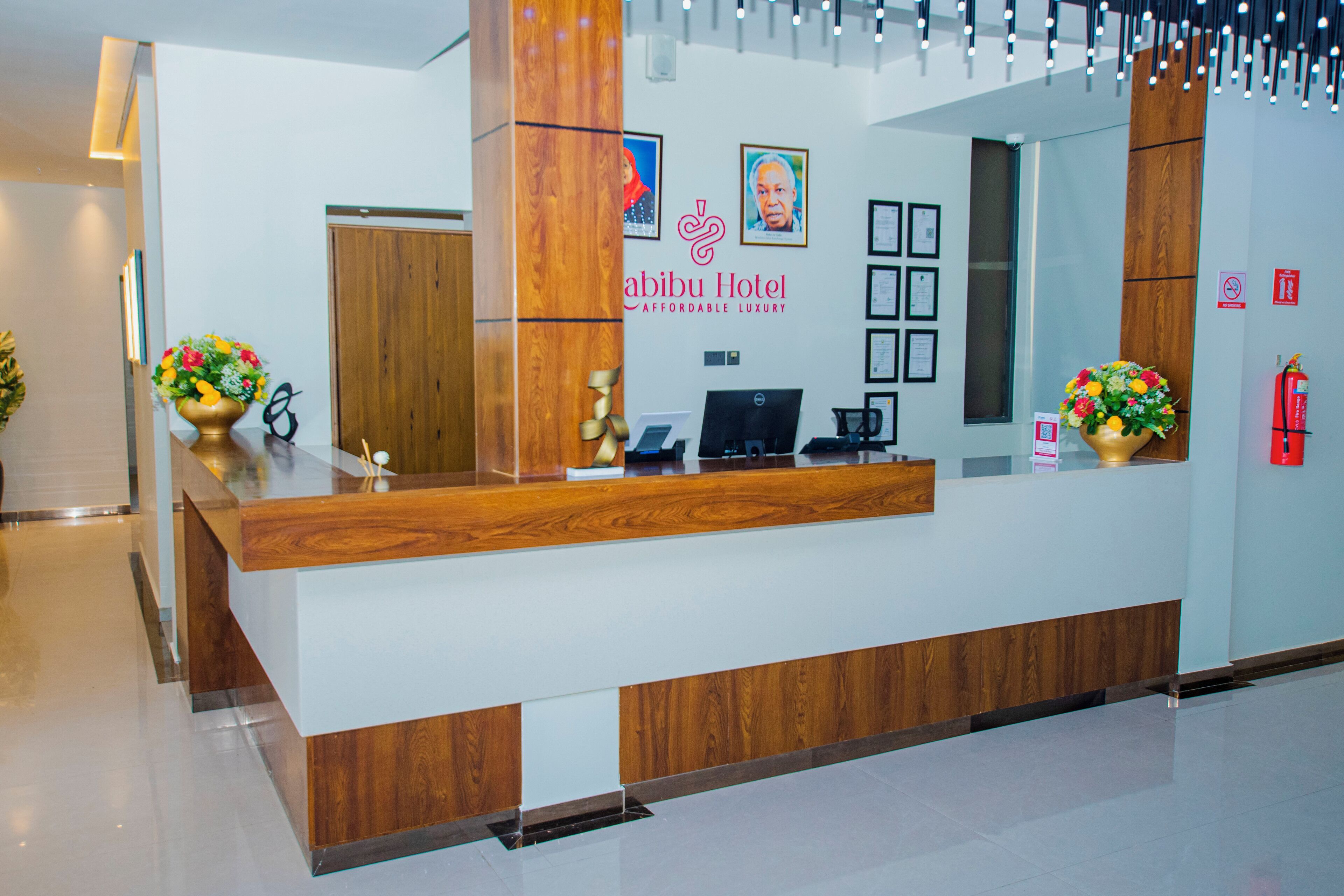 A hotel reception desk with a wooden finish, a digital screen, and framed certificates on the wall.