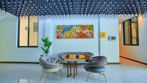 Eine moderne Lobby mit einem grauen Sofa, zwei Sesseln und einem kleinen Tisch. Ein farbenfrohes abstraktes Gemälde ziert die Wand, und ein Topf mit Pflanze ist sichtbar.